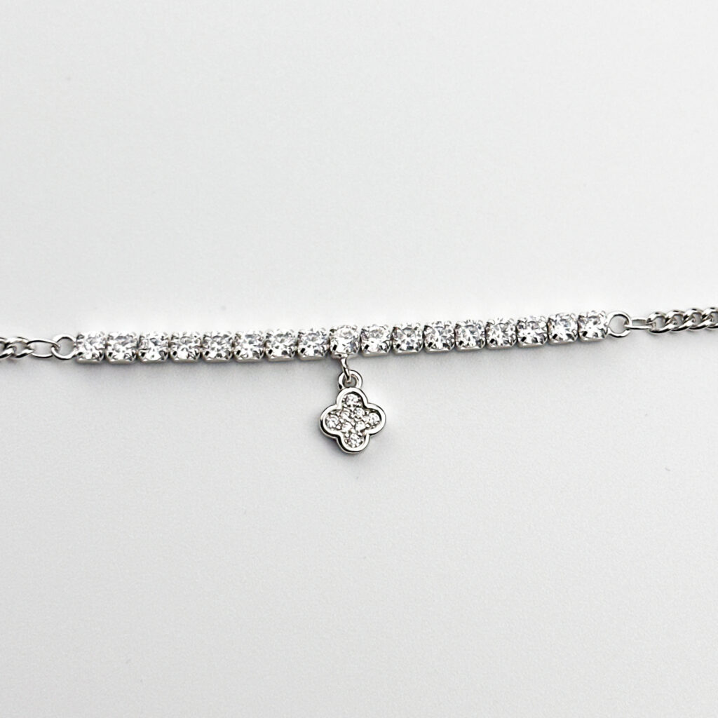 A silver tennis bracelet with cubic zirconia stones and a four-leaf clover charm.