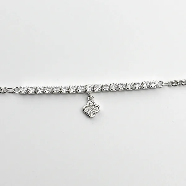 A silver tennis bracelet with cubic zirconia stones and a four-leaf clover charm.