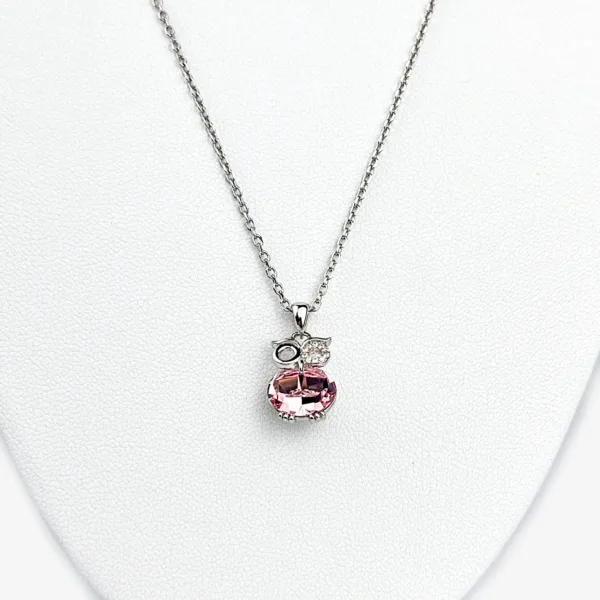 A silver necklace with a pink owl pendant adorned with clear gemstones, displayed on a white mannequin bust.