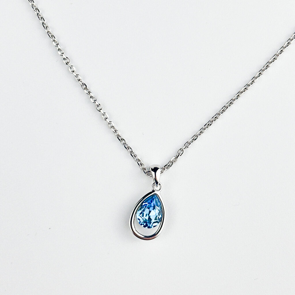 A silver chain necklace with a teardrop-shaped blue crystal pendant, displayed against a white background.