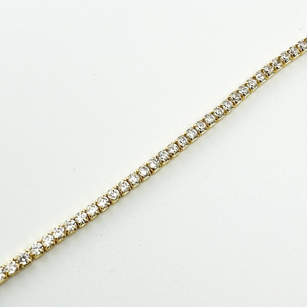 A gold tennis bracelet with round brilliant-cut diamonds on a white background.