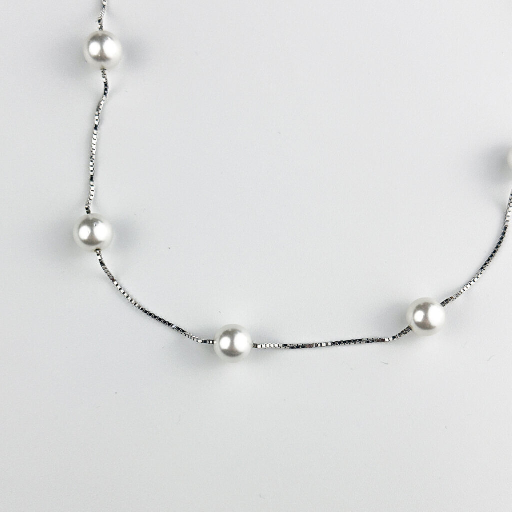 A silver box chain necklace with evenly spaced white pearls displayed against a white background.