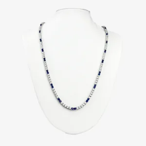 A silver tennis necklace with alternating small, round, clear gemstones and blue gemstones.