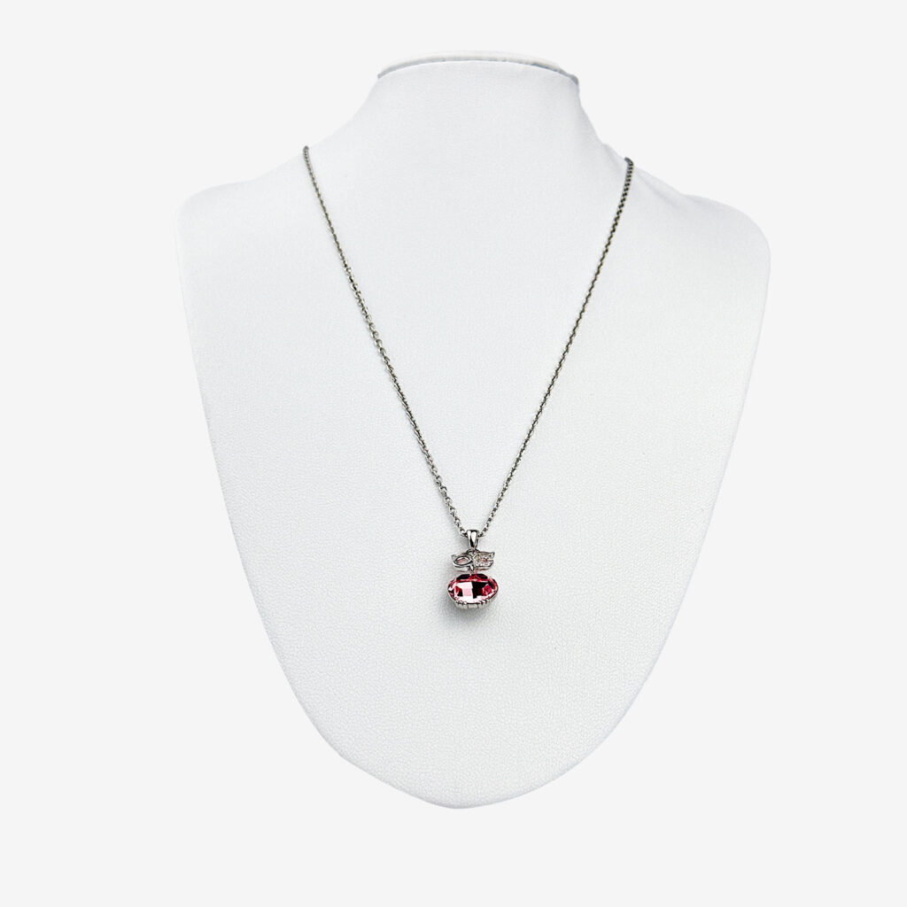 A silver chain necklace with a red oval pendant and a small rectangular accent, both adorned with clear gemstones. Displayed on a white mannequin bust.