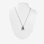 A silver chain necklace with a red oval pendant and a small rectangular accent, both adorned with clear gemstones. Displayed on a white mannequin bust.