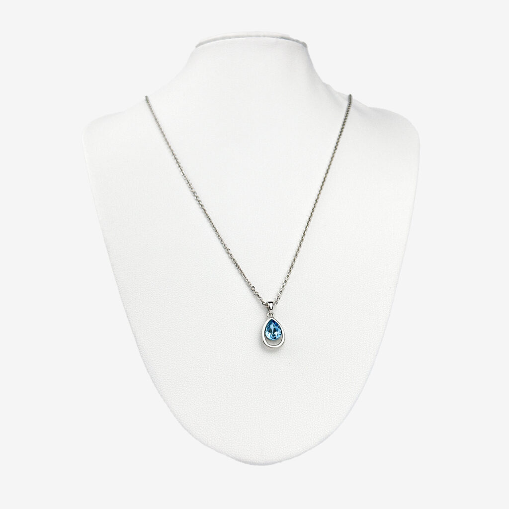 A silver chain necklace with a teardrop-shaped blue crystal pendant displayed on a white mannequin bust.