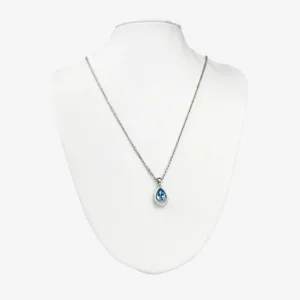 A silver chain necklace with a teardrop-shaped blue crystal pendant displayed on a white mannequin bust.