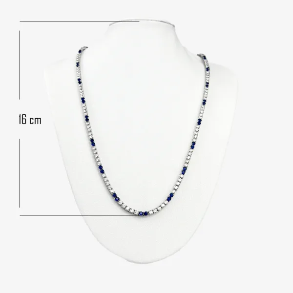 A silver tennis necklace with alternating small, round, clear gemstones and blue sapphires. The necklace is 16 cm long and is displayed on a white mannequin bust.