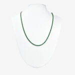 A silver tennis necklace with small, round emerald gemstones.