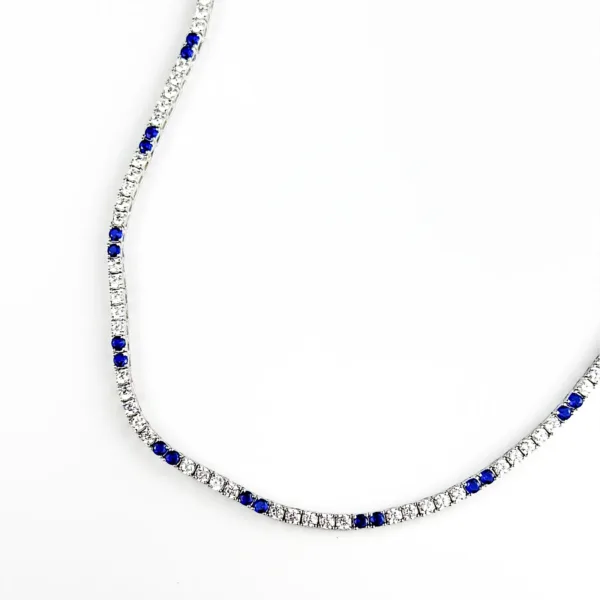 A silver tennis necklace with alternating small, round, clear gemstones and blue sapphires.